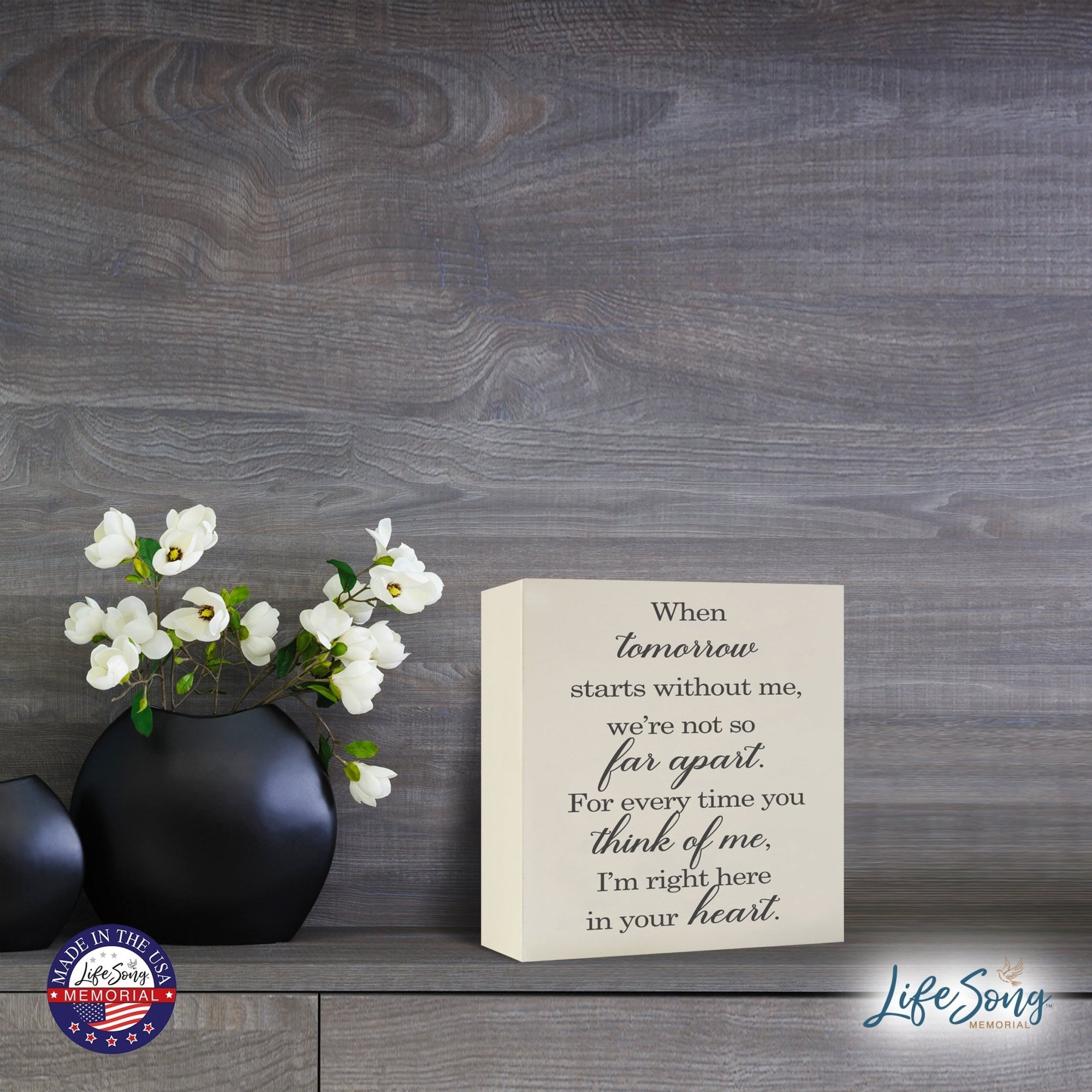 Lifesong Milestones Memorial Shadow Box Urn For Human Ashes showcased on a wooden tabletop, adorned with sophisticated black vases holding delicate white flowers, serving as a heartfelt keepsake with the touching message.